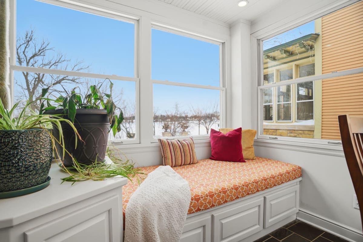 Your cozy window seat invites peaceful moments with vibrant pillows, soft throws, and winter views beyond the glass.