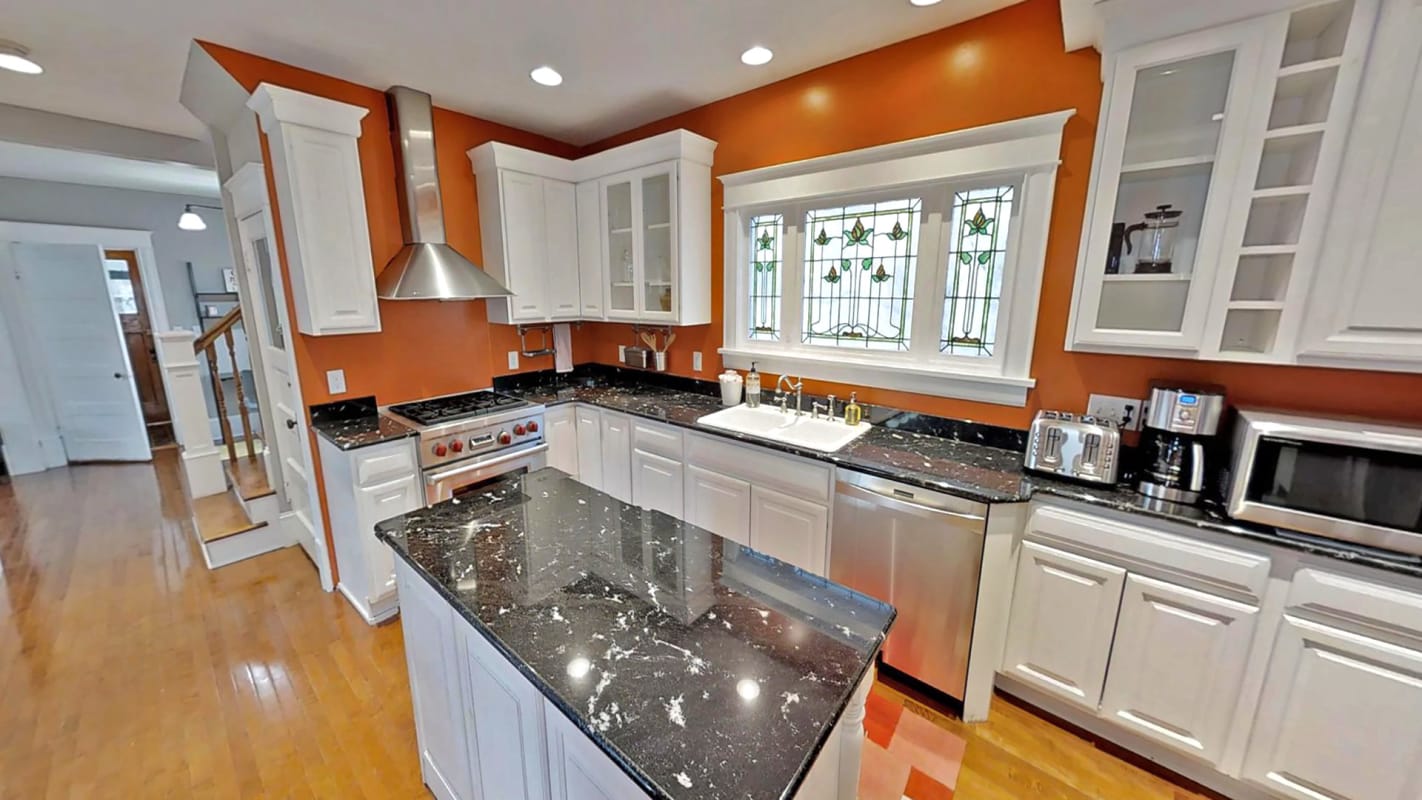 Your gourmet kitchen awaits with granite countertops, stainless steel appliances, and vibrant orange walls creating the perfect space for memorable meals.
