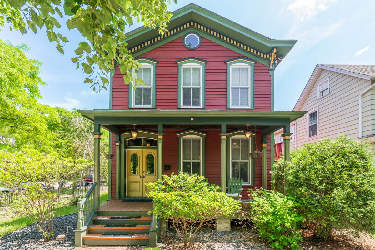 Charming Victorian home with red siding and green trim nestled in a tree-lined neighborhood, featuring welcoming front porch and period details.