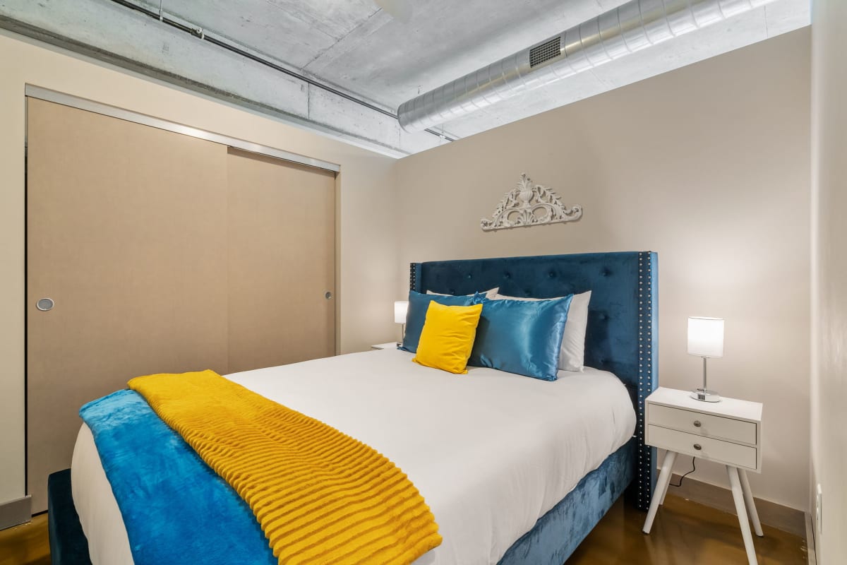 Sink into plush bedding with vibrant blue and yellow accents in your stylish bedroom featuring industrial-chic exposed ceilings.