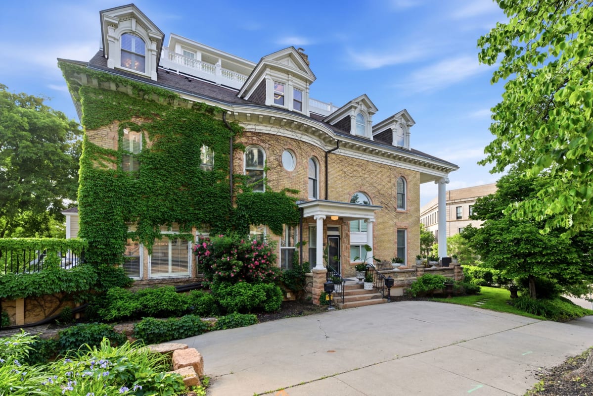 A historic brick property with ivy-covered walls, elegant architectural details, and a welcoming entrance surrounded by lush gardens and mature trees.