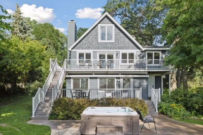 A charming lakeside home with multi-level decks, a private hot tub, and a serene, wooded backdrop.