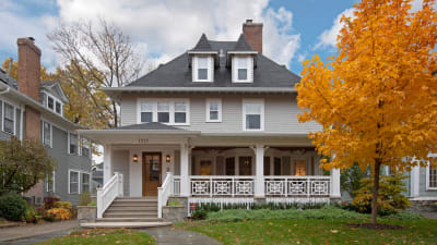 Two-story home with a wraparound porch and autumn foliage.