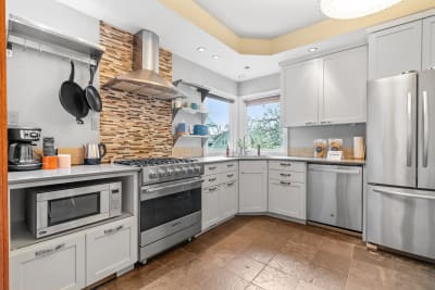 Spacious kitchen with stainless steel appliances, gray cabinets, and natural light from windows.