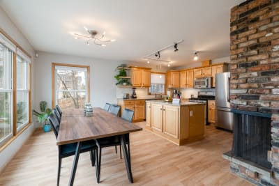 Open kitchen and dining area with wooden cabinets, dining table, and exposed brick fireplace.