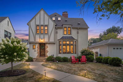 Tudor-style home with a lovely front lawn, red outdoor chairs, and warm lighting at dusk.