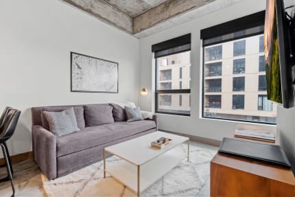 Stylish living room featuring a gray sofa, minimalist white table, and large windows overlooking city buildings.