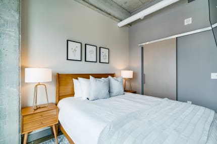 Modern bedroom with a wooden bed, grey throw pillows, and framed botanical prints.
