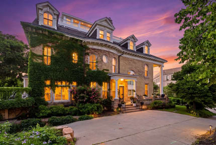 Victorian home with ivy and warm lights against a colorful sunset sky.