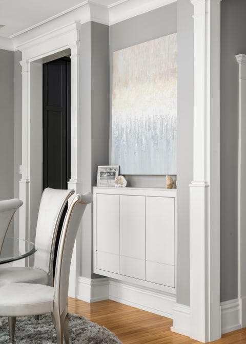 Elegant dining area showcasing gray walls, minimalist white storage, and an abstract artwork.
