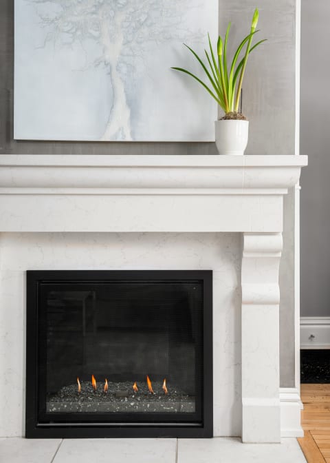 A modern marble fireplace with flickering flames, an abstract tree painting above, and a green plant in a white pot.