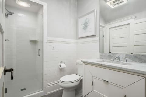 A modern bathroom with a glass shower, marble countertops, and white cabinetry.
