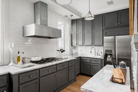 A sleek kitchen featuring dark gray cabinetry, marble countertops, and stainless steel appliances with natural light streaming in.