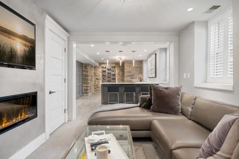 A sophisticated living area featuring a leather sectional sofa, electric fireplace, and modern kitchen with stone wall.