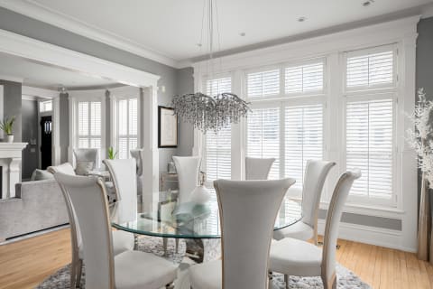 Elegant dining room featuring a glass round table, white chairs, and a crystal chandelier.
