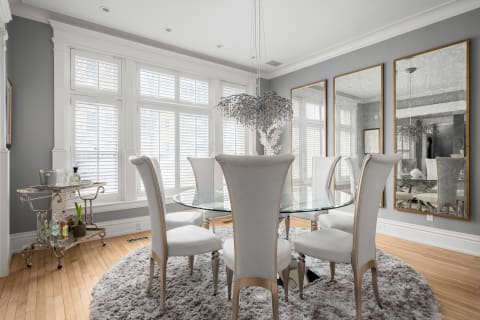 A bright, sophisticated dining room with a glass table, white chairs, and a chandelier, reflecting an airy ambiance.