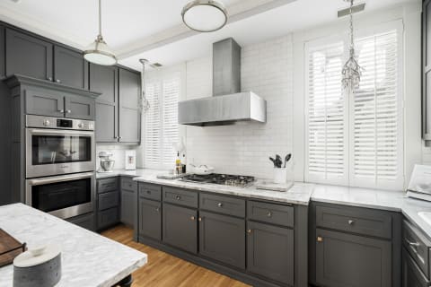 Modern kitchen with gray cabinets, marble countertops, and stainless steel appliances.