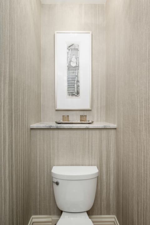 Elegant powder room with textured wallpaper, black and white artwork, and a marble shelf with candles.