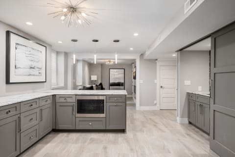 Modern kitchen with gray cabinets and marble countertops, illuminated by a starburst chandelier.
