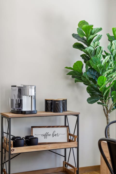 Coffee bar setup with an espresso machine, black mugs, labeled canisters, and a fiddle leaf fig plant.