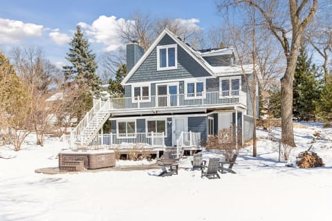 A gray A-frame house surrounded by snow with decks and outdoor seating.