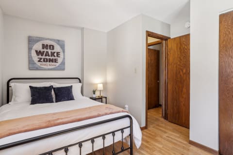 A serene bedroom featuring a comfortable bed, a quirky sign on the wall, and natural wood accents, ideal for restful nights.
