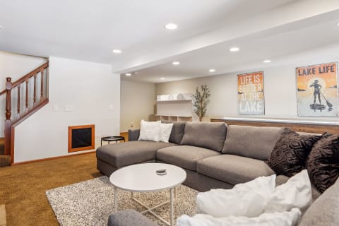 A modern living room featuring a gray sectional couch, round coffee table, lake-themed wall art, and warm lighting.