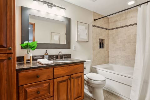 A cozy and elegant bathroom featuring wood cabinetry, a granite countertop, and a tub-shower combo with stylish stone tile accents.