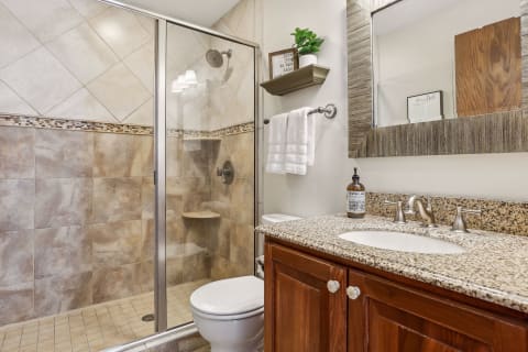 A modern bathroom featuring a glass-enclosed walk-in shower, granite countertop, and wooden cabinetry.