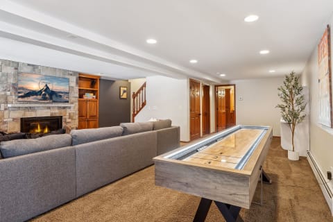 Cozy game room with a shuffleboard table, gray sectional couch, and a stone fireplace, creating a warm inviting atmosphere.