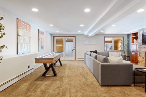 Spacious recreational room with a gray sectional sofa and shuffleboard table, adorned with lake-themed artwork.