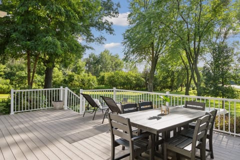 Spacious deck with dining table and lounge chairs overlooking a lush green landscape.