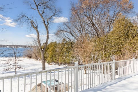 Winter waterfront view with snow-covered landscape and bare trees under a blue sky.