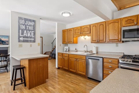 A spacious kitchen with wood cabinetry, stainless steel appliances, and a breakfast bar, adorned with a playful wall sign.