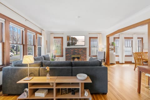 A spacious living room featuring a gray sectional sofa, brick fireplace, and large windows.