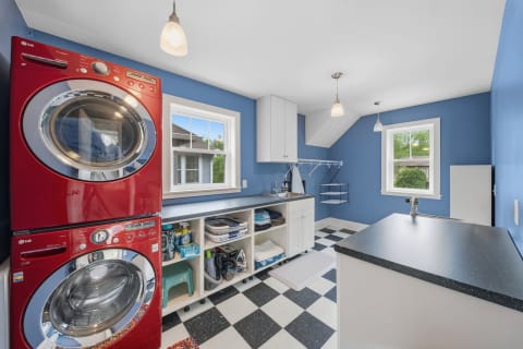 Modern laundry room featuring a stacked red washer and dryer, black and white checkered floor, and plenty of natural light.