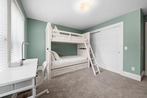 A bright children's room featuring a white bunk bed and a modern desk.