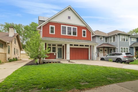 A red Craftsman-style home with a porch, attached garage, and a green lawn.