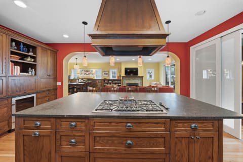 Spacious kitchen with gas cooktop island and wood cabinetry, connected to a colorful living room.