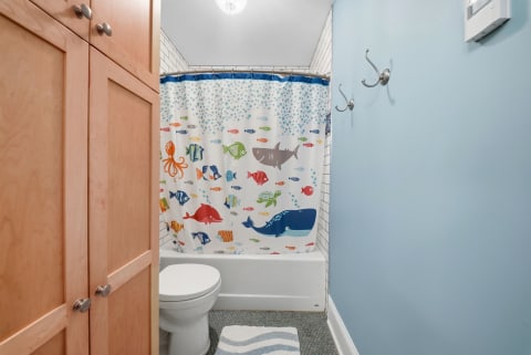 A family-friendly bathroom featuring an ocean-themed shower curtain, blue walls, and light wood cabinetry.