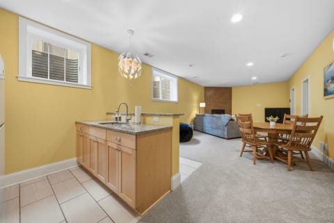 An inviting open area with a kitchenette, dining table, and a cozy seating setup, accented by warm yellow walls and natural light.
