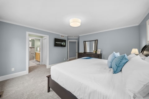 A stylish bedroom with calming blue-gray walls, plush bedding, and a flat-screen TV.