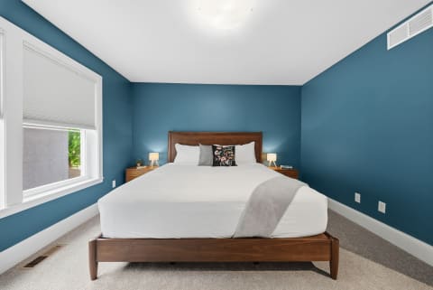 A tranquil bedroom featuring a cozy bed with white linens, blue walls, and wooden nightstands with lamps.
