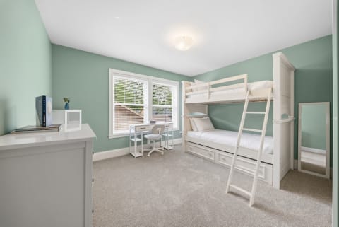 A serene children's room featuring a white bunk bed, workspace, and calming green walls.