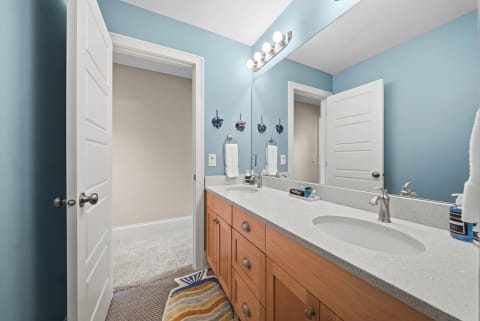 Coastal-inspired bathroom with dual sinks, soft blue walls, and plush flooring.