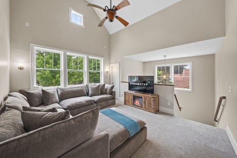 Bright living room featuring plush gray sofas, large windows, and a cozy electric fireplace.