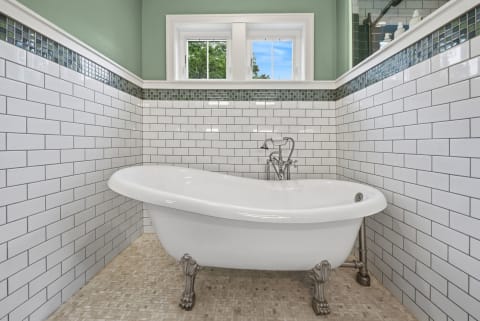 Clawfoot bathtub in a serene bathroom with white subway tiles and green accents, bathed in natural light.