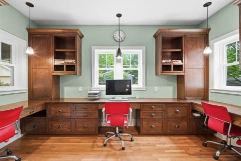 A beautifully designed workspace featuring wooden built-ins, two red chairs, and a view of the garden outside.