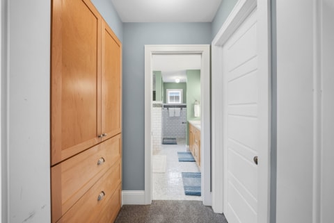 A hallway with custom cabinetry on the left leading to a bright bathroom with green walls and white tiles.