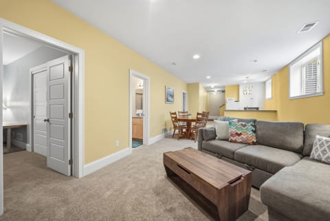 A cozy open living area with plush sectional sofa, golden walls, and a round dining table, showcasing a bright and inviting ambiance.